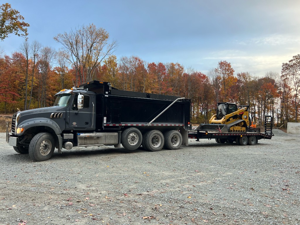 GHJ Excavation dump truck and CAT skid steer loader on a gravel job site with fall foliage in Western Pennsylvania